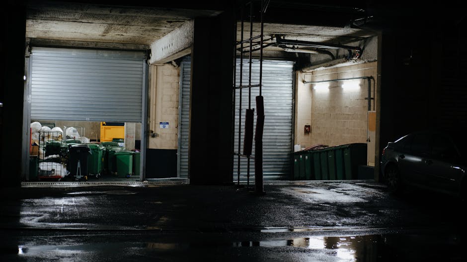 The image depicts a disorganized pile of discarded household items and debris placed on a paved outdoor area, likely part of a garden or driveway, adjacent to a brick wall. Prominently, there are two 